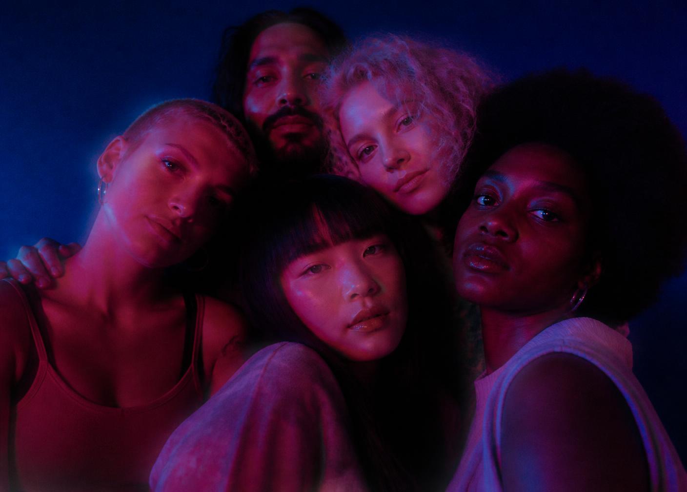 People of different cultures standing close together, lit in cyan and magenta